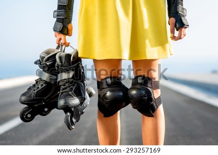 Sport woman in yellow skirt and protection wear holding rollers on the highway. Close up view on the knee and hands with rollers