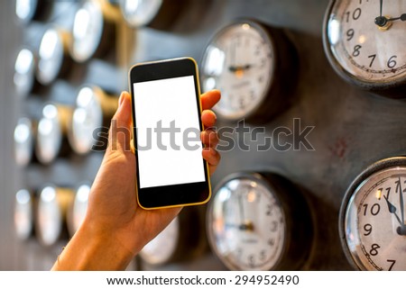 Female hand holding phone with white screen and metal clocks on background. Time phone application concept