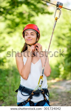 Young and pretty woman in red helmet preparing to ride on a zip line in the forest. Active sports kind of recreation
