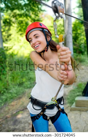 Young and pretty woman in red helmet enjoying riding a zip line in the forest. Active summer sports recareation