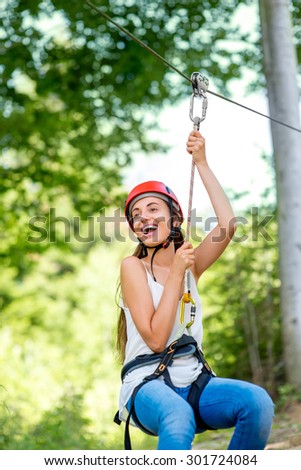 Young and pretty woman in red helmet riding on a zip line in the forest. Active sports kind of recreation