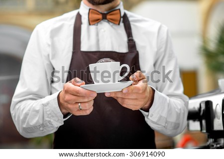 Barista in the brown apron holding white coffee cup in the cafe