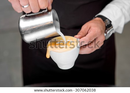 Barista making cappuccino with art shape on the dark apron background