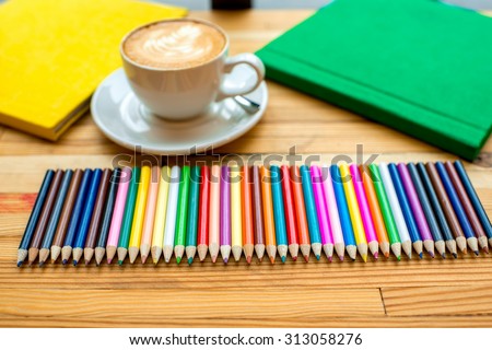 Group of colorful pencils with coffee cup and books on the wooden table