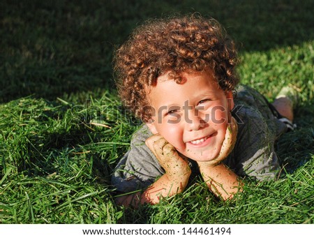 Happy kid with curly hair lying on a pile of fresh green cut grass
