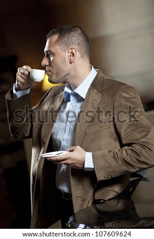 Man dressed on suite drinks cup of coffee inside hotel lobby.