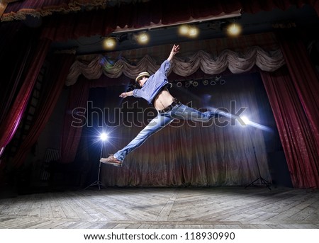 Modern ballet style male dancer performs on high lighted stage .