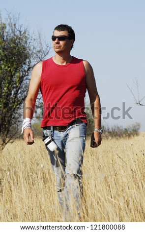 Yang and confident man walks through tall dry grass.