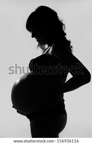 Silhouette of pregnant woman Silhouette in gray background of pregnant woman that holds her belly with her hand