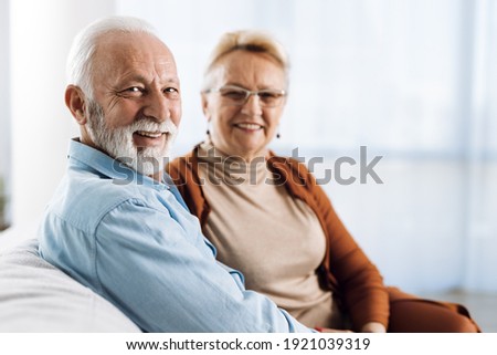 Smiling senior couple  sitting at home. There are looking at camera