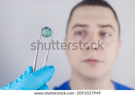 Conceptual shot of an eye crystalline lens replacement. Ophthalmic surgery. Return of sight. Removal of cataracts. Surgical intervention in the eyeball. Doctor holds the implant near the patient Photo stock © 