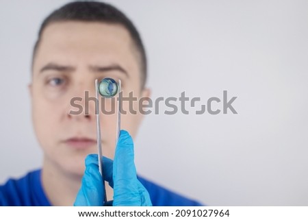 Conceptual shot of an eye crystalline lens replacement. Ophthalmic surgery. Return of sight. Removal of cataracts. Surgical intervention in the eyeball. Doctor holds the implant near the patient Photo stock © 