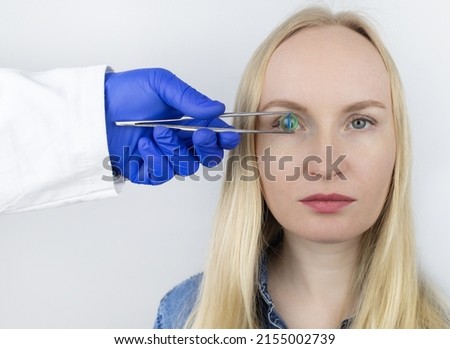 Conceptual shot of an eye crystalline lens replacement. Ophthalmic surgery. Return of sight. Removal of cataracts. Surgical intervention in the eyeball. Doctor holds the implant near the patient Foto d'archivio © 