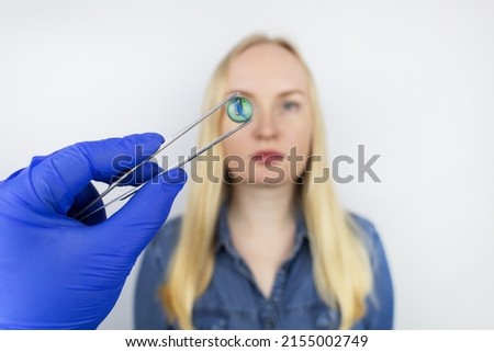 Conceptual shot of an eye crystalline lens replacement. Ophthalmic surgery. Return of sight. Removal of cataracts. Surgical intervention in the eyeball. Doctor holds the implant near the patient Foto d'archivio © 
