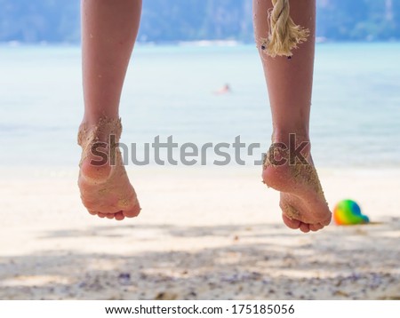 Legs of  caucasian girl, child, kid  on swing at the trpoical beach