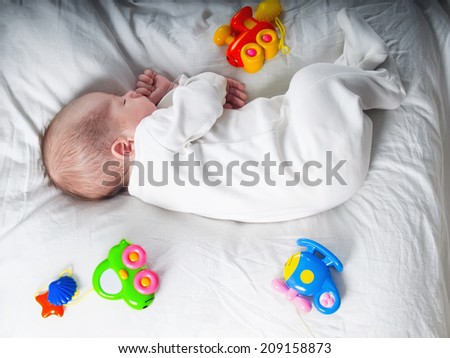 Caucasian newborn baby toddler boy sleeping in his bed with toys