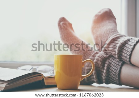 Woman resting keeping legs in warm socks on table with morning coffee and reading book 商業照片 © 