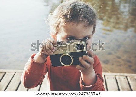 Portrait of a smiling cute boy taking picture with retro camera at a lake