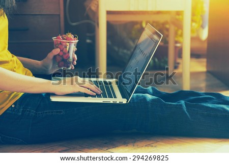 Hands using laptop and typing with glass of strawberry on wooden floor at home