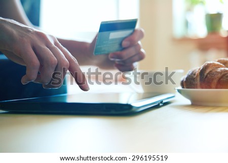 Hands holding credit card and using digital tablet pc with morning coffee and croissant. Online shopping.