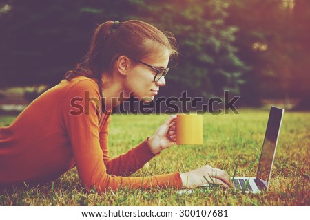 girl lying on the grass and using laptop and typing with coffee or tea mug