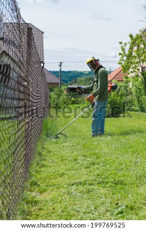 Male worker with power tool string lawn trimmer mower cutting grass. Health and safety concept.