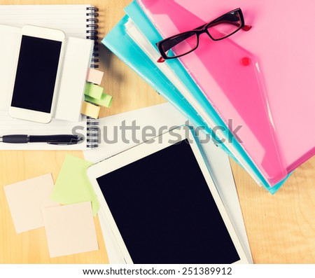 Messy office table with digital tablet, smartphone, reading glasses, notepad and filling folders. View from above with copy space