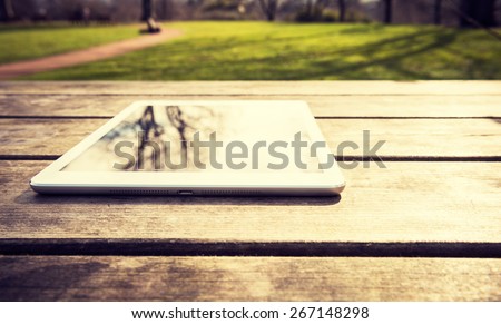 Rustic wooden table with digital tablet and trees reflecting on black screen. View from above with copy space