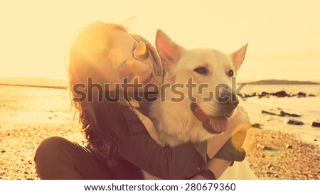Hipster girl playing with dog at a beach during sunset, strong lens flare effect