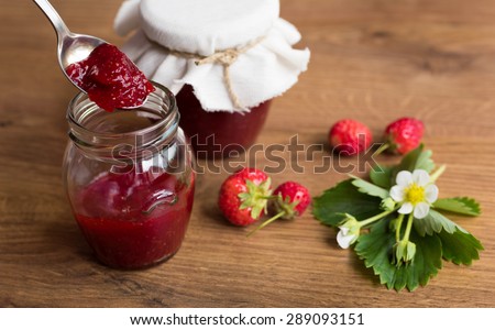 Homemade strawberry jam (marmalade) in jars on wooden background.