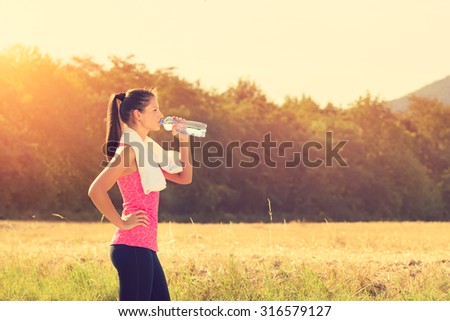 Attractive female taking a break after jogging, holding bottle of water