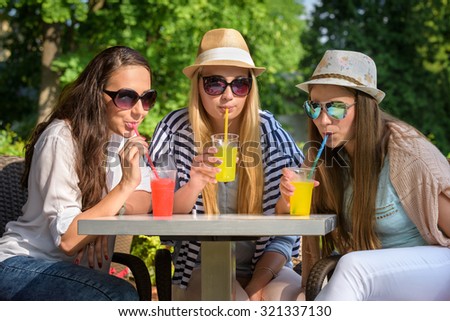 Three attractive girlfriends enjoying cocktails in an outdoor cafe, friendship concept