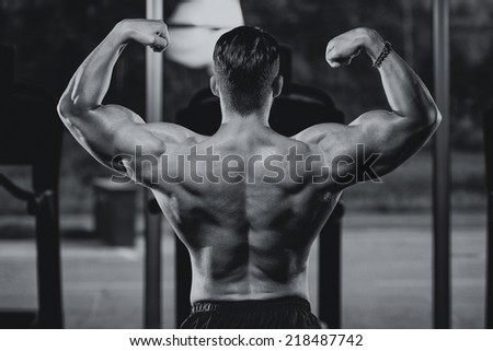 Serious Man Bodybuilder Standing In The Gym And Flexing Muscles