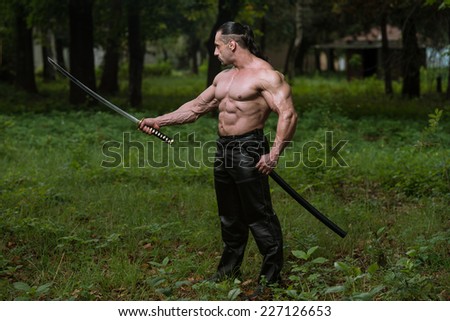Muscular Man Holding Ancient Sword - Standing In Forest Wearing Leather Pants