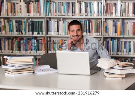 In The Library - Handsome Male Student With Laptop And Books Working In A High School - University Library - Shallow Depth Of Field