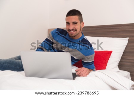 Young Man Lying On Bed And Having Fun With Laptop In Bedroom