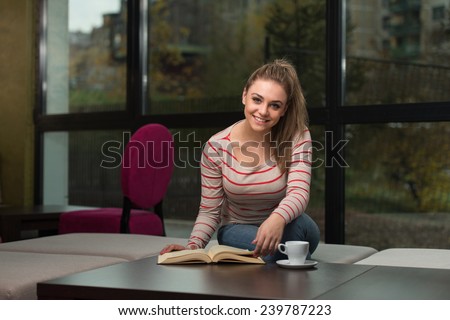 Young Female Student Drinking And Reading Book In Cafeteria