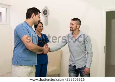 Smiling Doctor Takes The Patient\'s Dentist And Shakes His Hand In His Medical Dental Office - Doctor Wearing Medical Clothing