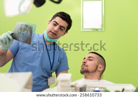 Dentist , Assistant And Patient Looking At Tooth X-Ray