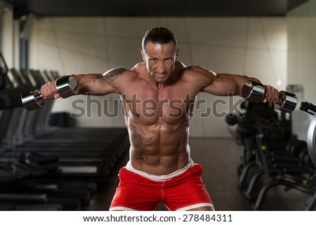 Muscular Mature Man Doing Heavy Weight Exercise For Shoulders With Dumbbells In Modern Fitness Center
