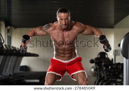 Muscular Mature Man Doing Heavy Weight Exercise For Shoulders With Dumbbells In Modern Fitness Center