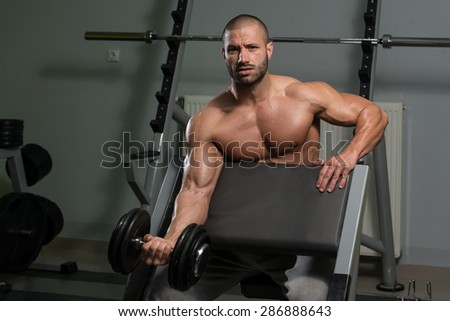 Muscular Young Man Doing Heavy Weight Exercise For Biceps With Dumbbell In Gym