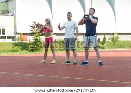 Group Of Young People Doing A Kettle Bell Exercise Outdoor With Instructor