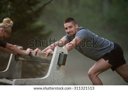Young Couple Stretching Before Running In Wooded Forest Area - Training And Exercising For Trail Run Marathon Endurance - Fitness Healthy Lifestyle Concept