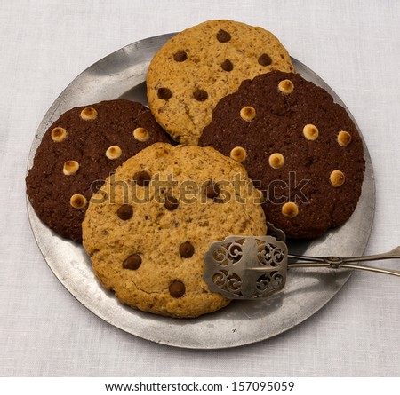White and dark chocolate chip cookies on tin plate with serving scissors on white canvas