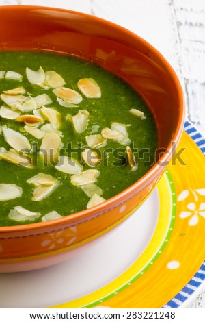 Swiss chard and potato cream soup with chopped roasted almonds in brown ceramic bowl