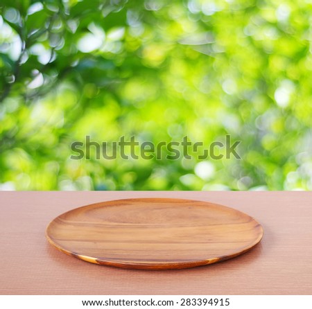 Empty round wooden tray on table over blur tree background, for product display montage