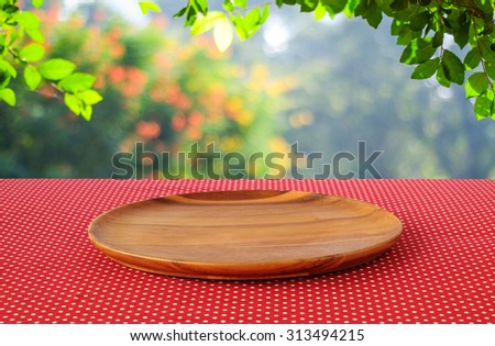 Empty round wooden tray on red polka dot tablecloth over blur trees with bokeh background, Product display montage