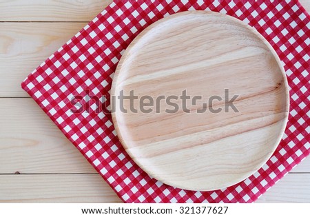 Empty round wooden plate on red check tablecloth background, top view, food display montage