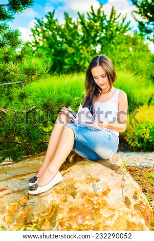 Young woman sitting on a stone and reading a book